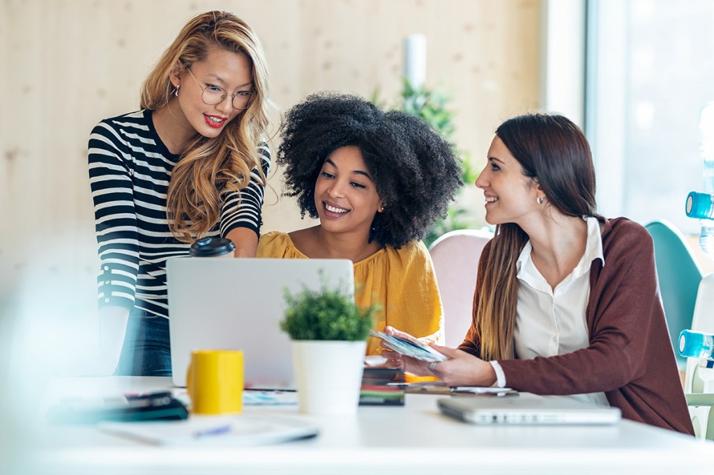 Image shows three business women having a meeting around a laptop in a coworking office